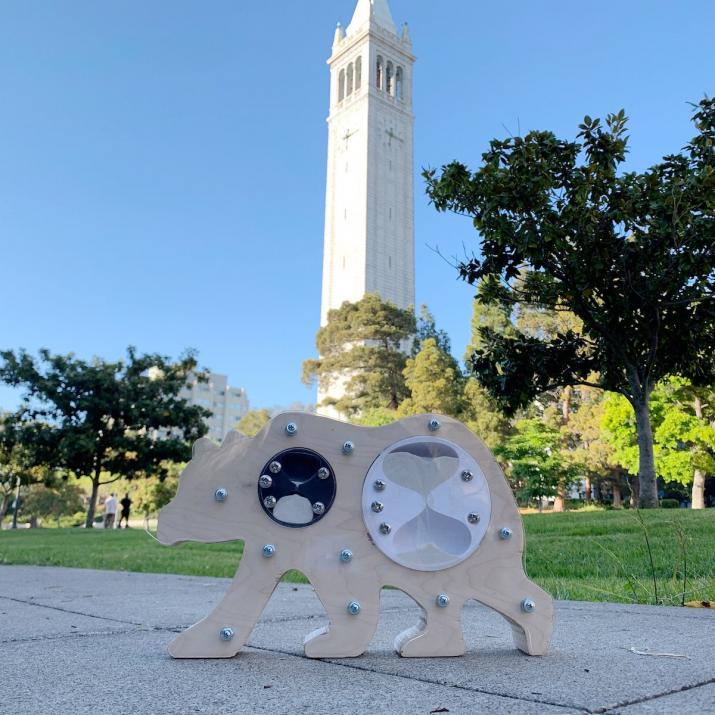 Pomodoro bear made of wood and glass rests on a sidewalk with the Campanile in the background.