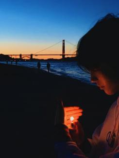 Person cups the flames from a lighter with their hand during sunset, with the Golden Gate Bridge in the background.