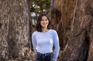 Flora Huynh poses for a portrait in a blue top in front of Eucalyptus trees.